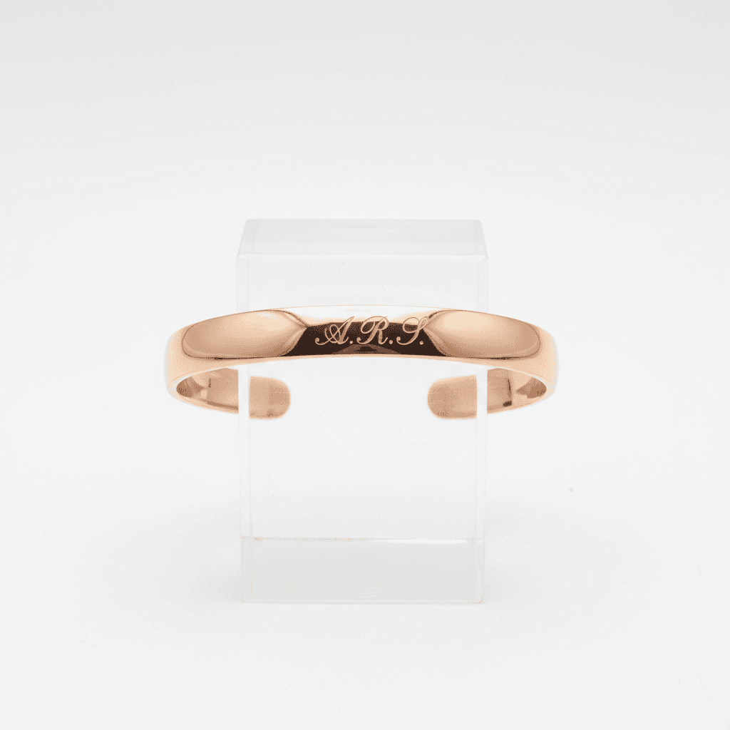 Polished rose gold open cuff bracelet engraved with initials A.R.S. on acrylic display