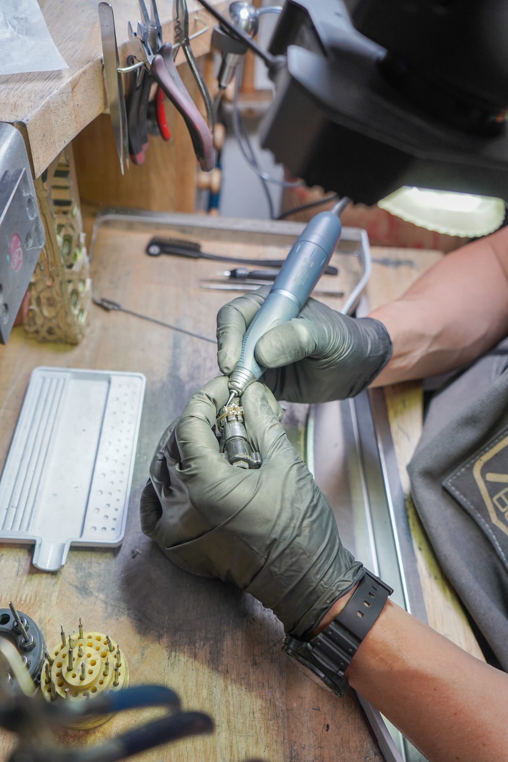 Jeweler in black gloves using a rotary tool to polish a gold ring at a workbench