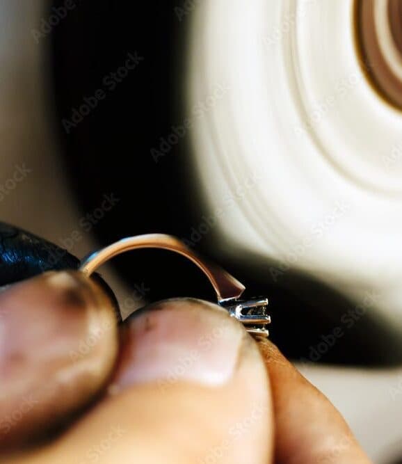 Jeweler's hands holding a gold ring with prong setting against a spinning polishing wheel