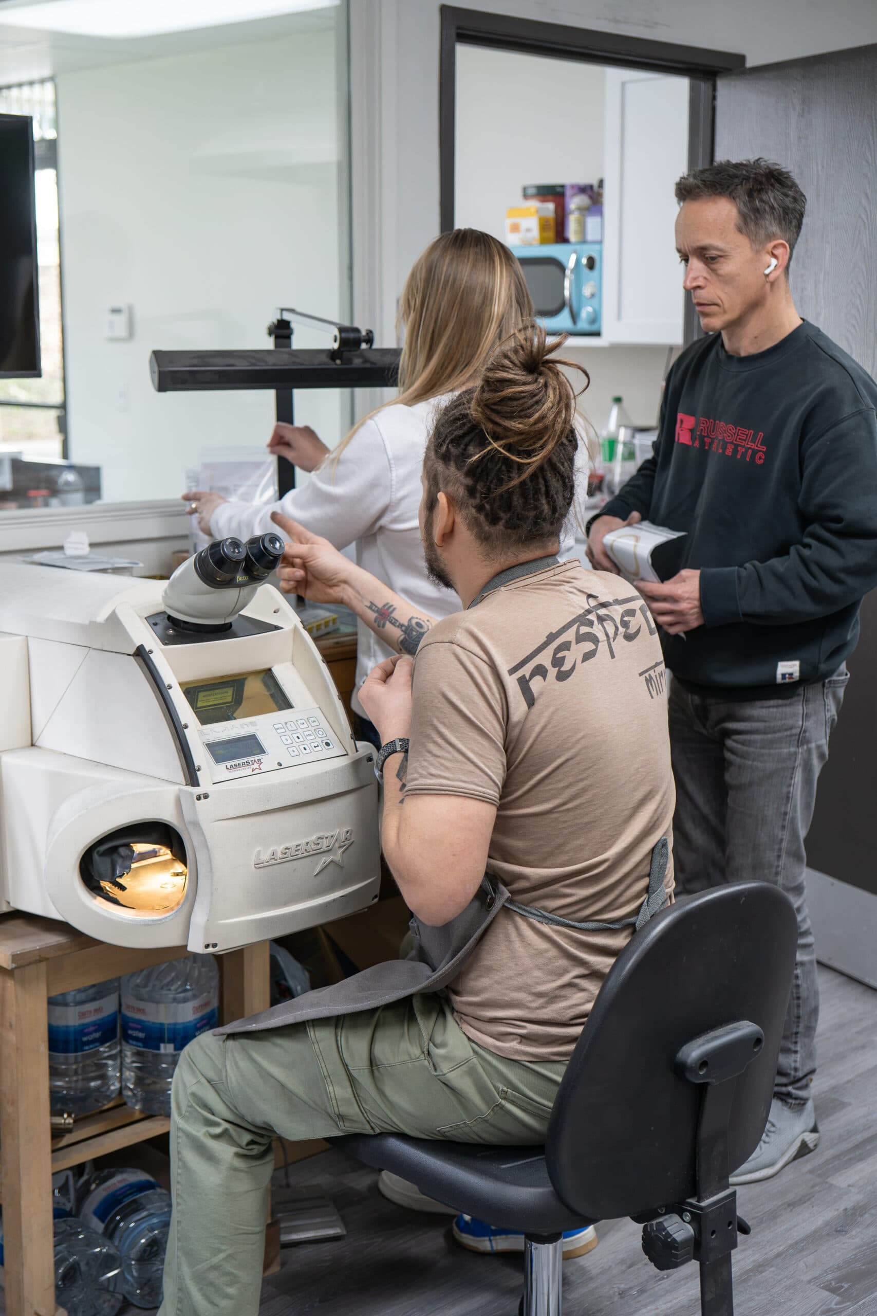 Three jewelers working around a LaserStar laser welding machine in a workshop