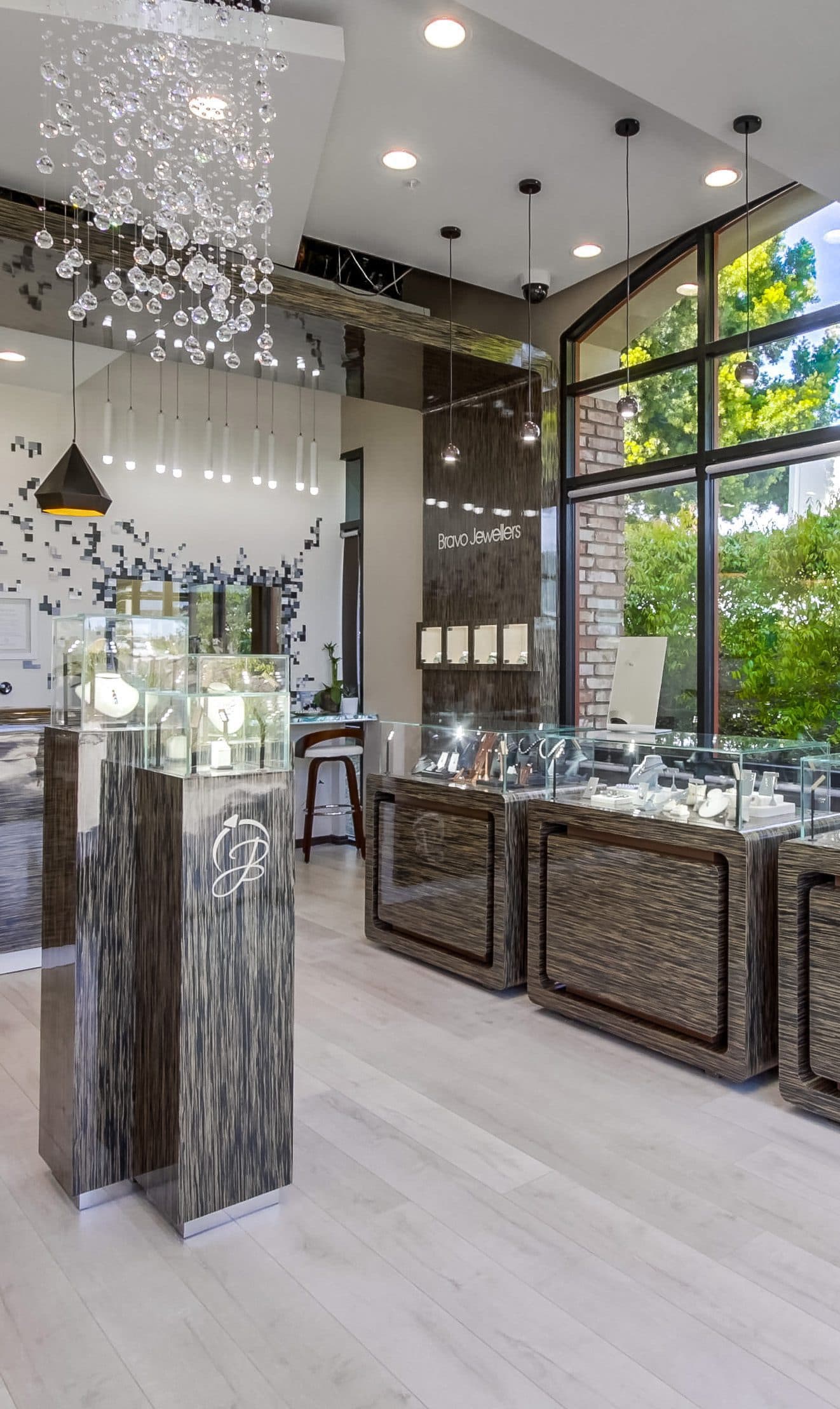 Modern jewelry store interior, glass display cases, crystal chandelier, wood-tone pedestals, Bravo Jewellers signage.