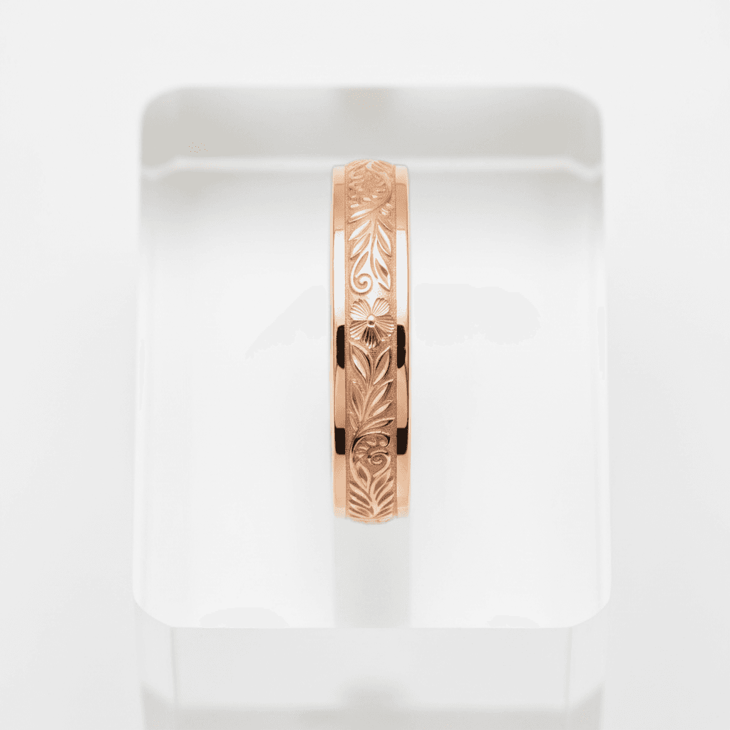Rose gold band ring with engraved floral and leaf scrollwork pattern on display stand