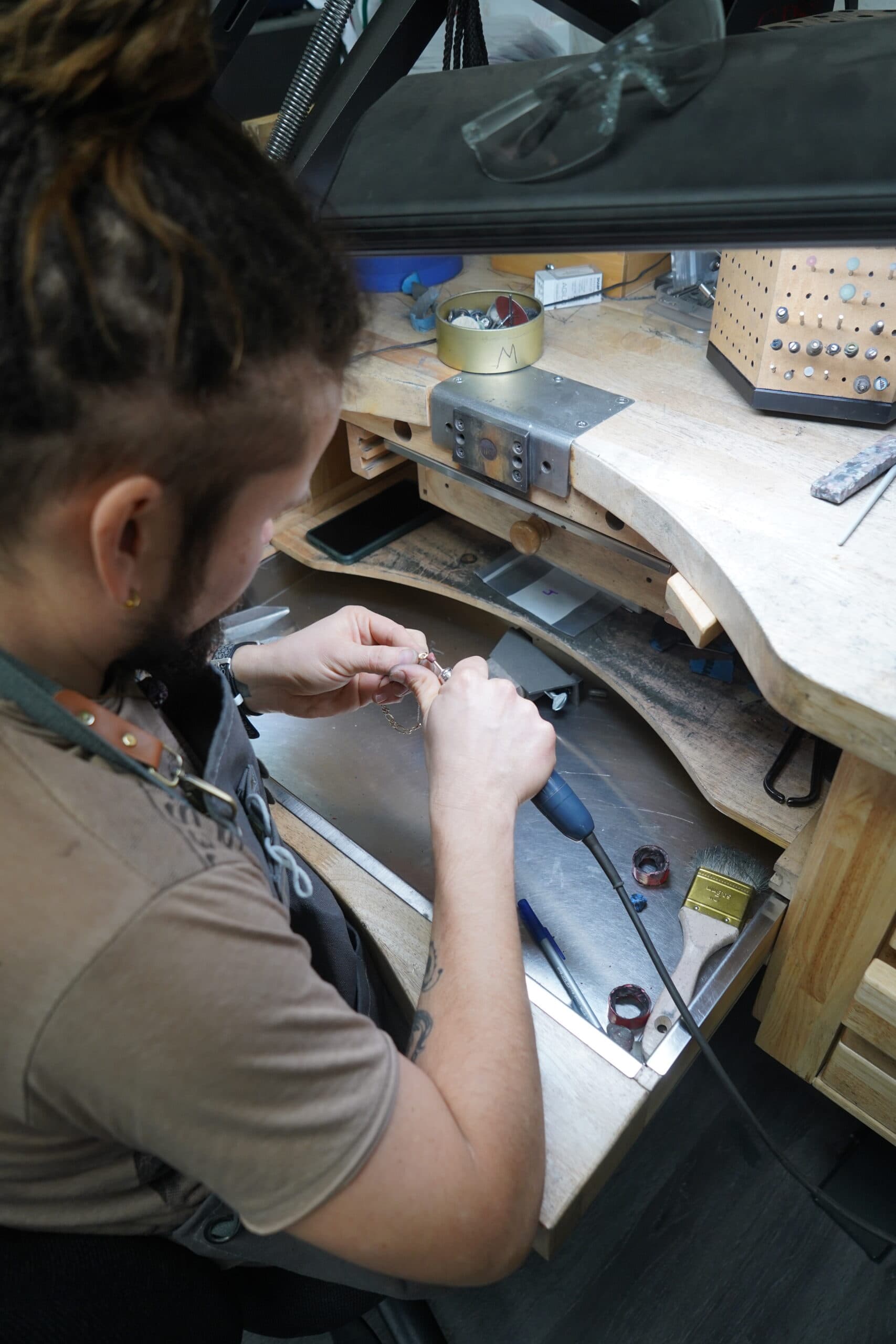 Jeweler in leather apron carefully assembling a delicate ring at a wooden workbench