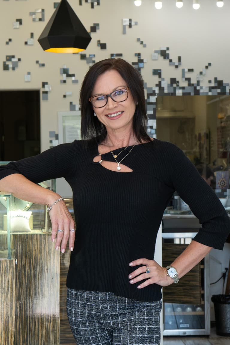 Smiling woman wearing layered necklaces, rings, and a silver bracelet inside a jewelry store