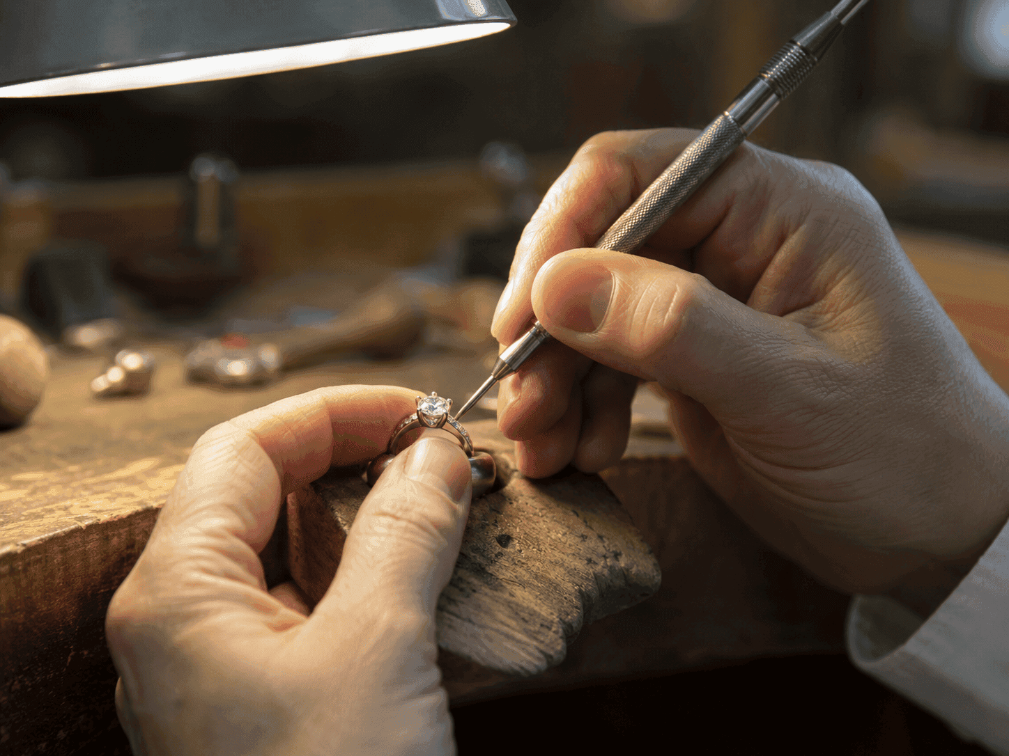 Jeweler setting round diamond solitaire engagement ring, white metal, prong setting, wooden workbench workshop.