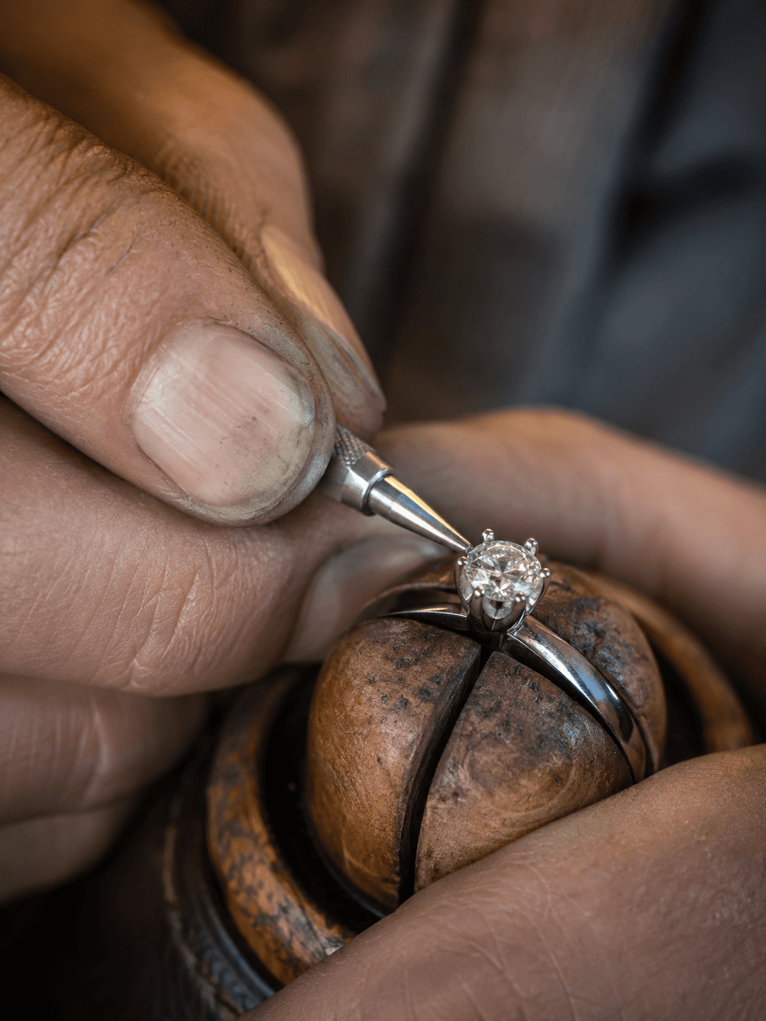 Jeweler's hands using a fine tool to set a round diamond in a silver prong ring